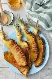 Photo of Tasty grilled pineapples, honey and wooden spoon on light gray tiled table, flat lay