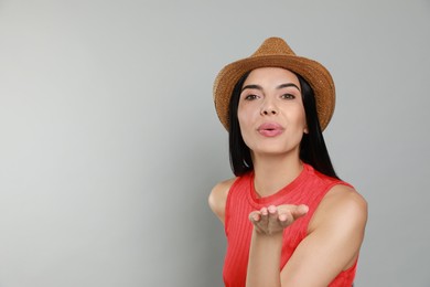 Photo of Beautiful young woman with straw hat blowing kiss on light grey background. Space for text