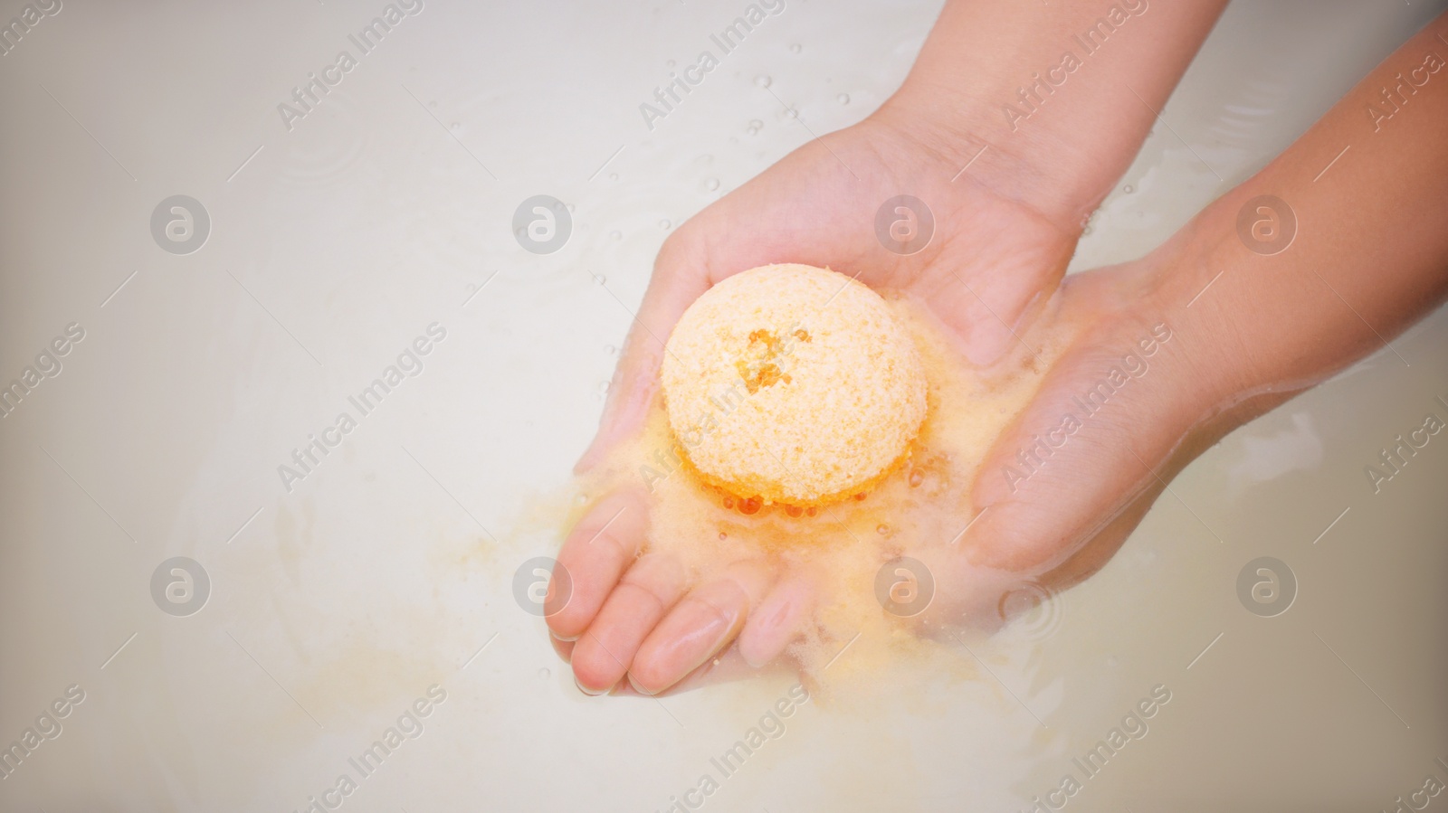 Photo of Woman holding bath bomb over water with foam, above view. Space for text