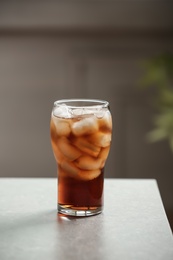 Photo of Glass of cola with ice on table against blurred background, space for text