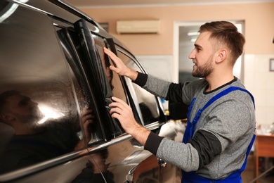 Photo of Worker tinting car window with foil in shop