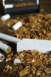 Photo of Tobacco and hand rolled cigarettes on wooden table, closeup