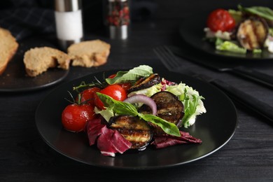 Photo of Delicious salad with roasted eggplant and basil served on black wooden table