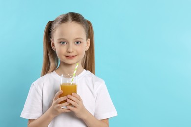 Photo of Cute little girl holding glass of fresh juice with straw on light blue background, space for text