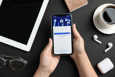 Photo of MYKOLAIV, UKRAINE - JULY 9, 2020: Woman holding Iphone 11 with Facebook app on screen at black table, top view