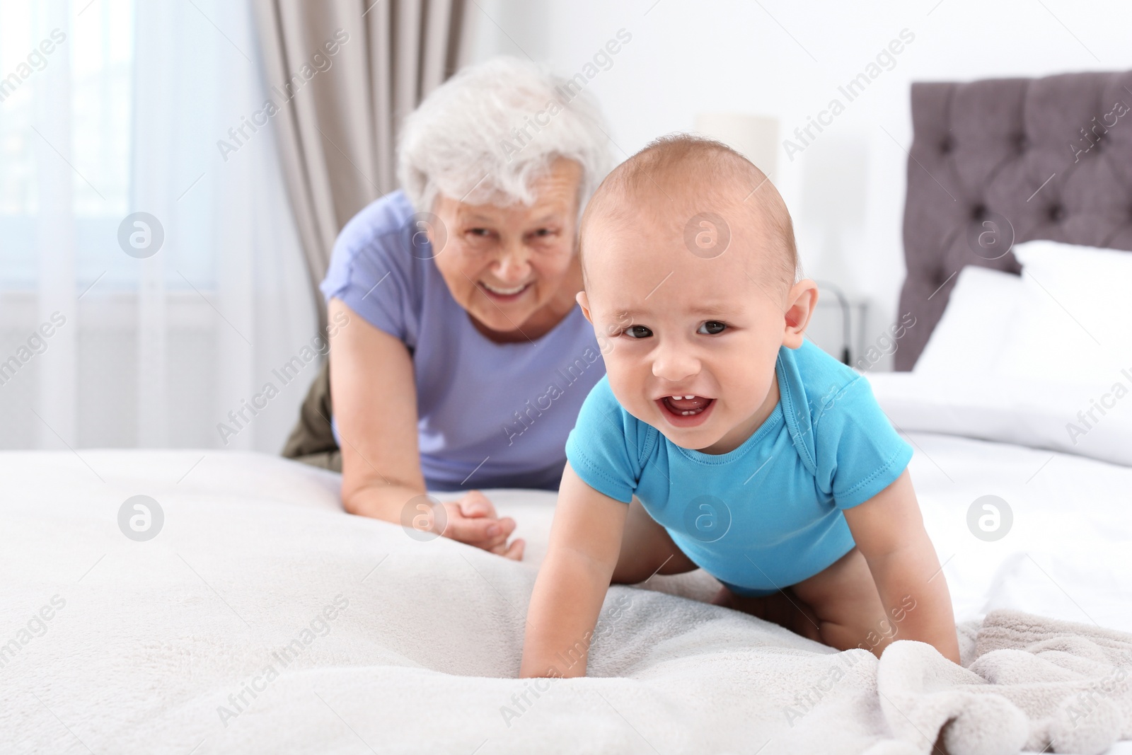 Photo of Cute little baby with happy grandmother in bedroom
