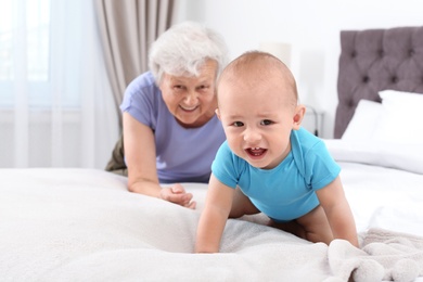 Photo of Cute little baby with happy grandmother in bedroom