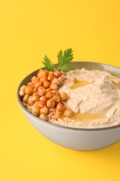 Photo of Bowl of tasty hummus with chickpeas and parsley on yellow background