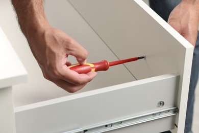 Photo of Man with screwdriver assembling drawer indoors, closeup
