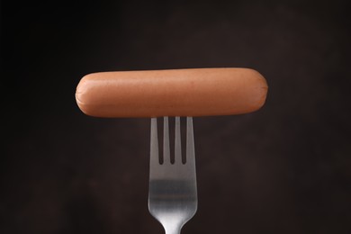 Photo of Delicious boiled sausage on fork against dark background, closeup