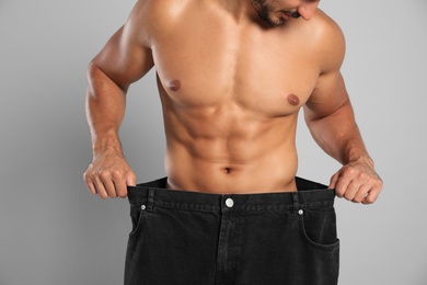 Photo of Young man with slim body in old big size jeans on grey background, closeup view