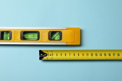 Photo of Building level and tape measure on light blue background, top view. Space for text