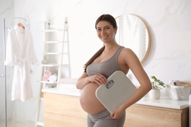 Photo of Young pregnant woman with scales in bathroom