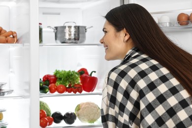 Photo of Young smiling woman looking into modern refrigerator
