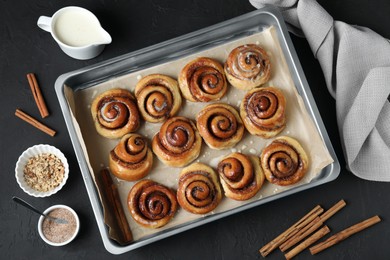 Photo of Tasty cinnamon rolls in baking dish on black wooden table, flat lay