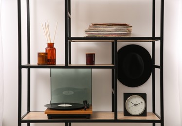 Photo of Stylish turntable with vinyl record on shelving unit indoors