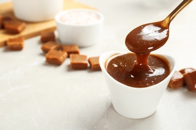 Photo of Spoon with tasty caramel sauce over bowl on table. Space for text