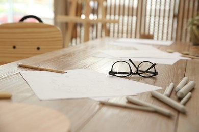 Photo of Male portrait drawing, pencils and glasses on wooden table in art studio