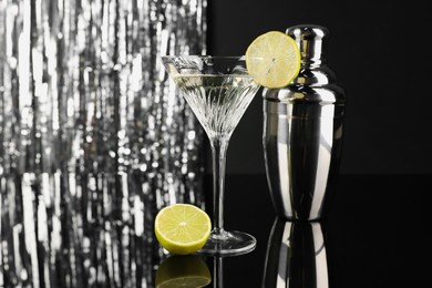 Photo of Martini cocktail with lemon slice and shaker on black and silver background