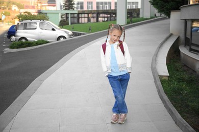 Photo of Cute little girl with backpack on city street. Space for text