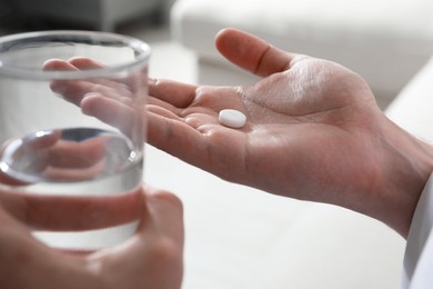 Photo of Man with glass of water and pill on blurred background, closeup