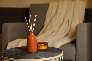 Photo of Aromatic reed air freshener and scented candle on table indoors