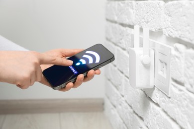 Image of Woman with smartphone connecting to internet via wireless repeater indoors, closeup. Wi-Fi symbol on device screen