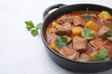 Photo of Delicious goulash in pot on white tiled table, closeup. Space for text