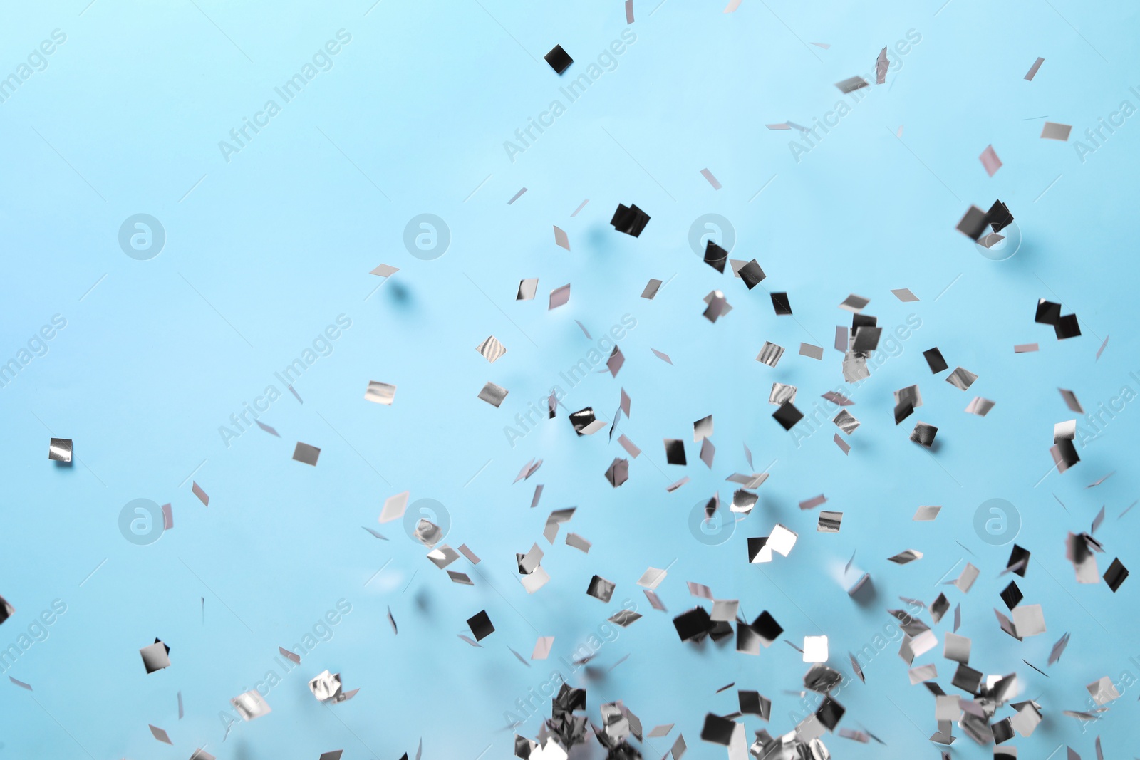 Shiny pink confetti falling down on light blue background Photo of Shiny pink confetti falling down on light blue background