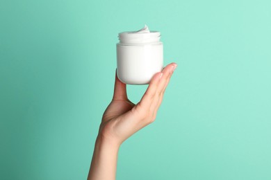 Photo of Woman holding jar of face cream on light turquoise background, closeup