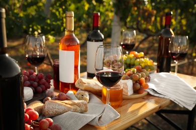 Photo of Red wine and snacks served for picnic on wooden table outdoors