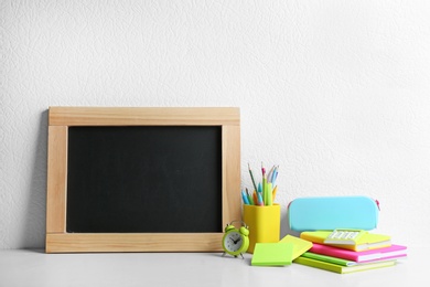 Photo of Blank small chalkboard and different school stationery on wooden table near white wall. Space for text