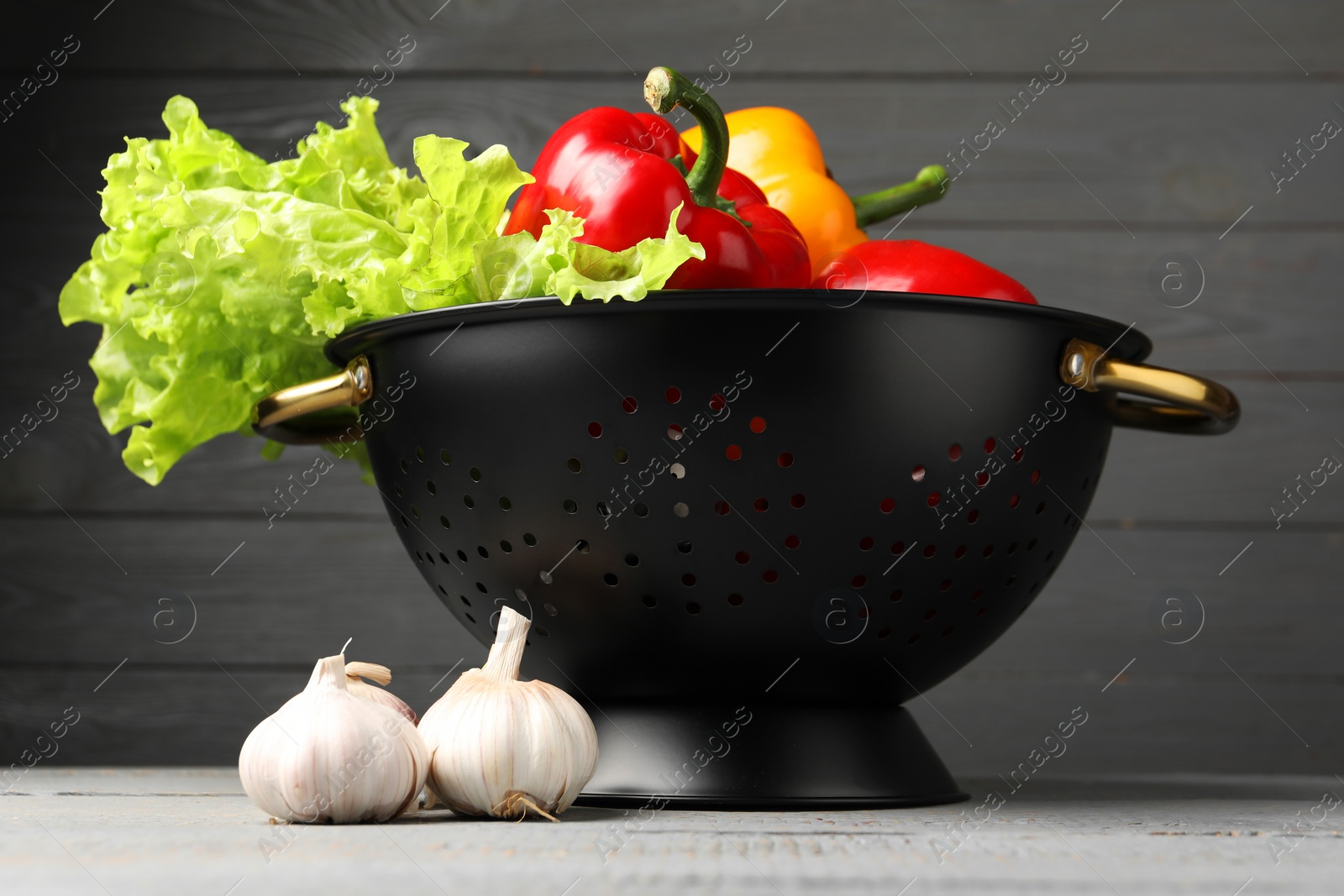 Photo of Black colander and different vegetables on rustic wooden table, closeup