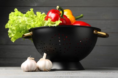 Photo of Black colander and different vegetables on rustic wooden table, closeup