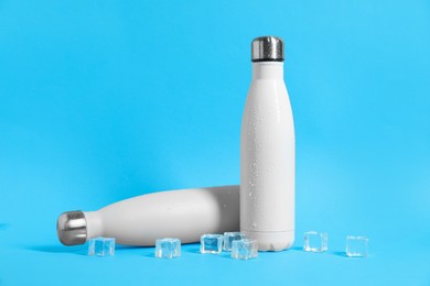 Photo of Stylish thermo bottles with water drops and ice cubes on light blue background, space for text