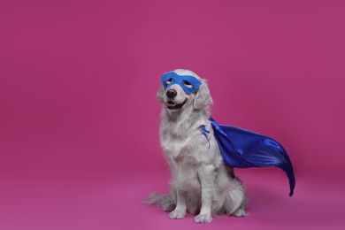 Photo of Adorable dog in blue superhero cape and mask on pink background, space for text