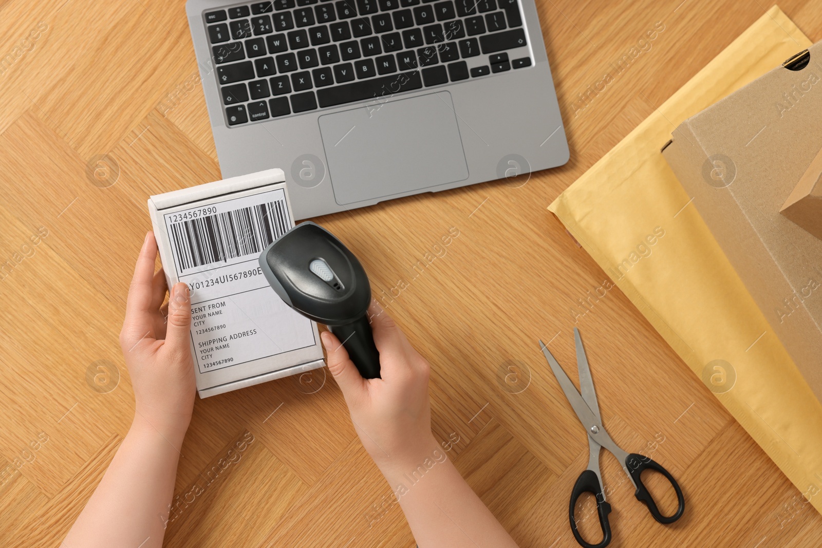 Photo of Woman with scanner reading parcel barcode at wooden table, top view. Online store