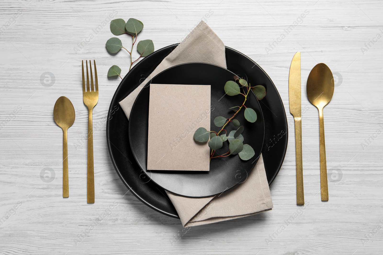 Photo of Stylish table setting with cutlery, blank card and eucalyptus leaves, flat lay