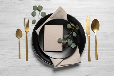 Photo of Stylish table setting with cutlery, blank card and eucalyptus leaves, flat lay