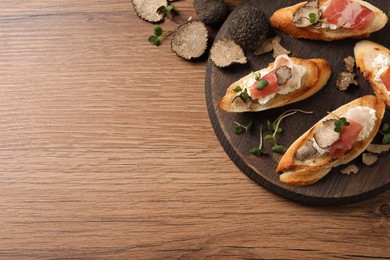 Photo of Delicious bruschettas with cheese, prosciutto and slices of black truffle on wooden table, flat lay. Space for text