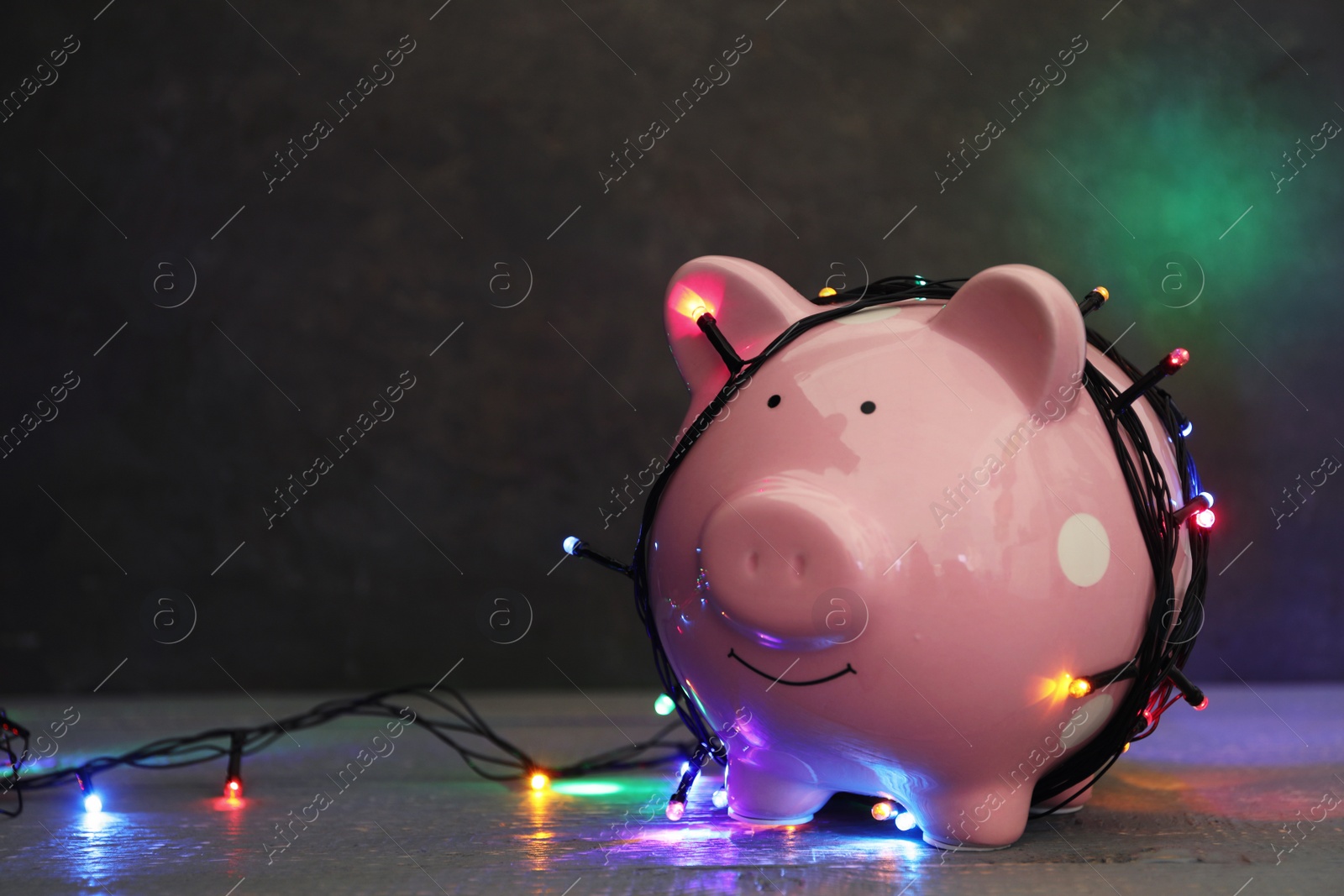 Photo of Piggy bank with Christmas lights on wooden table. Space for text