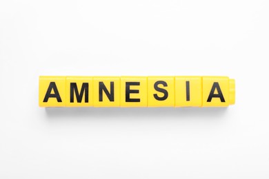 Photo of Yellow cubes with word Amnesia on white background, top view
