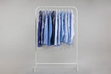 Photo of Dry-cleaning service. Many different clothes in plastic bags hanging on rack against grey background