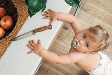 Photo of Little child near light countertop with knife, above view. Dangers in kitchen