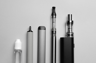 Photo of Different electronic cigarettes and liquid solution on light background, flat lay