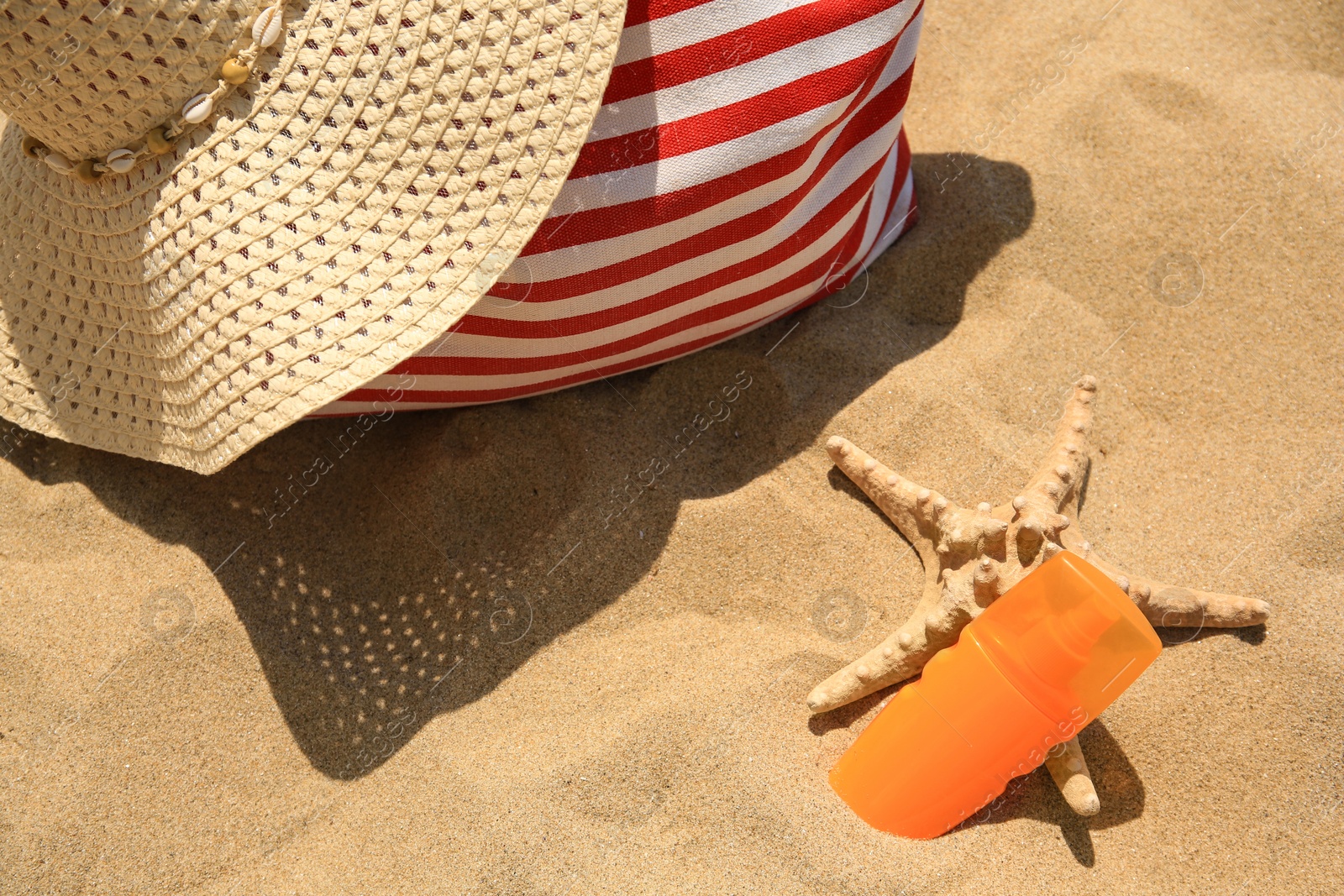 Photo of Bottle of sunscreen, starfish, bag and hat on sand, above view. Sun protection care