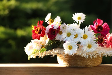 Photo of Beautiful wild flowers in wicker basket on wooden table against blurred background