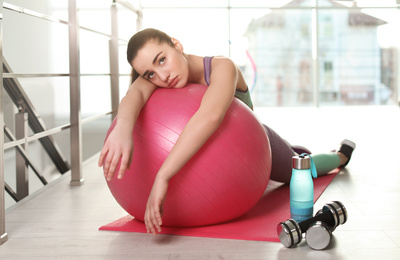 Photo of Lazy young woman with exercise ball on yoga mat indoors