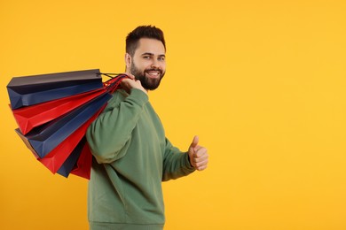 Photo of Happy man with many paper shopping bags showing thumb up on orange background. Space for text