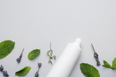 Photo of Blank tube of toothpaste, mint, thyme and lavender flowers on white background, flat lay. Space for text